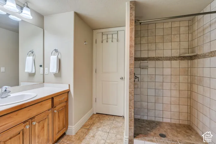 Walk-in shower with tiled walls and floor, vanity with wood cabinetry, and a countertop with an integrated sink