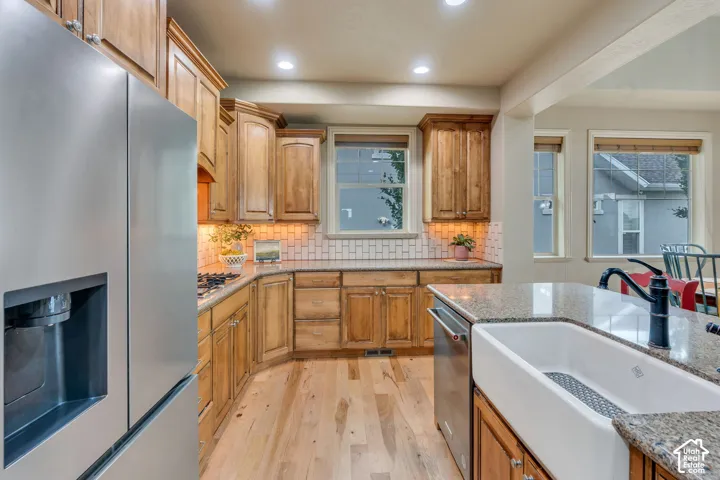 Kitchen featuring wood cabinetry, stainless steel appliances, a subway tile backsplash, and an island with an undermount farmhouse sink and granular stone countertop