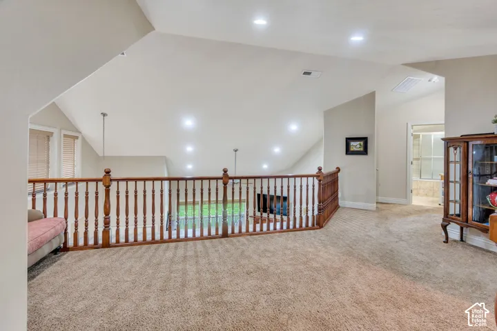 Carpeted loft space featuring vaulted ceilings, recessed lighting, and wood balustrade overlooking lower level