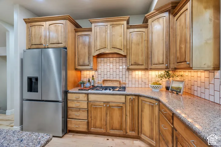 Stainless steel refrigerator, wood-finish cabinetry, subway tile backsplash, and light-toned countertops