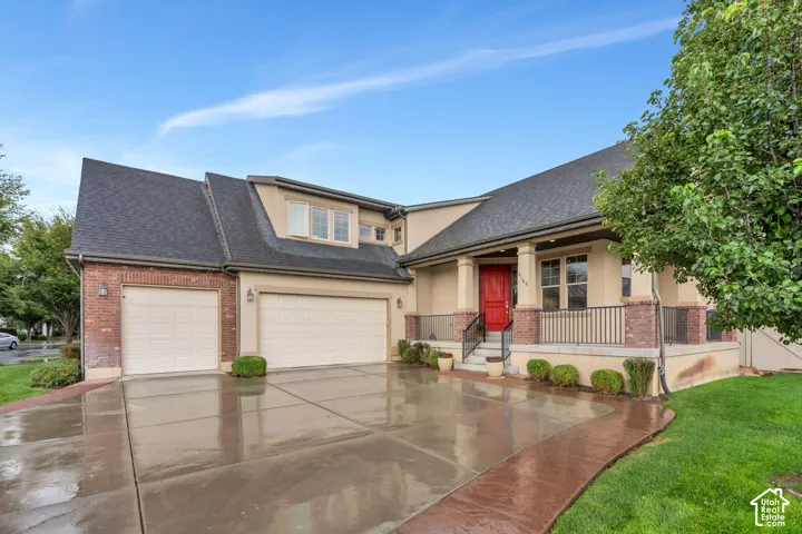 Stucco and brick exterior with a prominent red entry door, covered porch with columns, black iron railing, and two garage doors