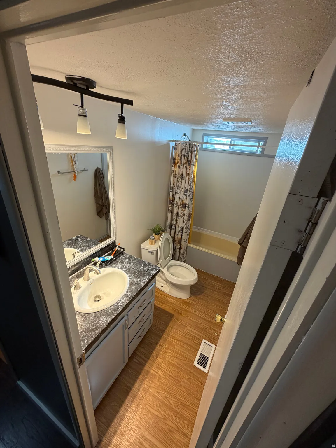 Bathroom featuring wood-finish flooring, a vanity with a counter and integrated sink, a toilet, and a bathtub with shower