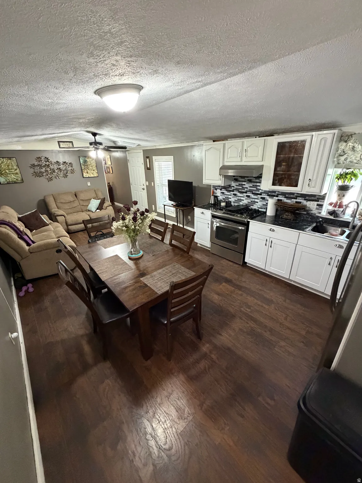 Open-concept living area featuring wood-finish flooring, white cabinetry, tile backsplash, and stainless steel appliances