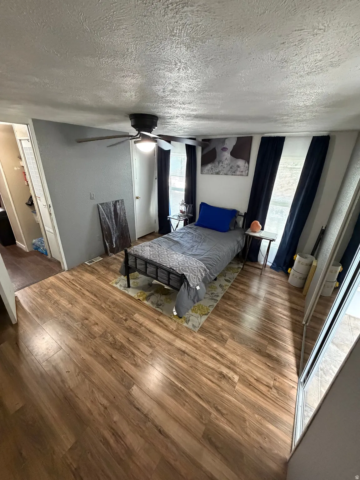 Wood-finish flooring, ceiling fan with integrated lighting, and multiple windows with curtain rods