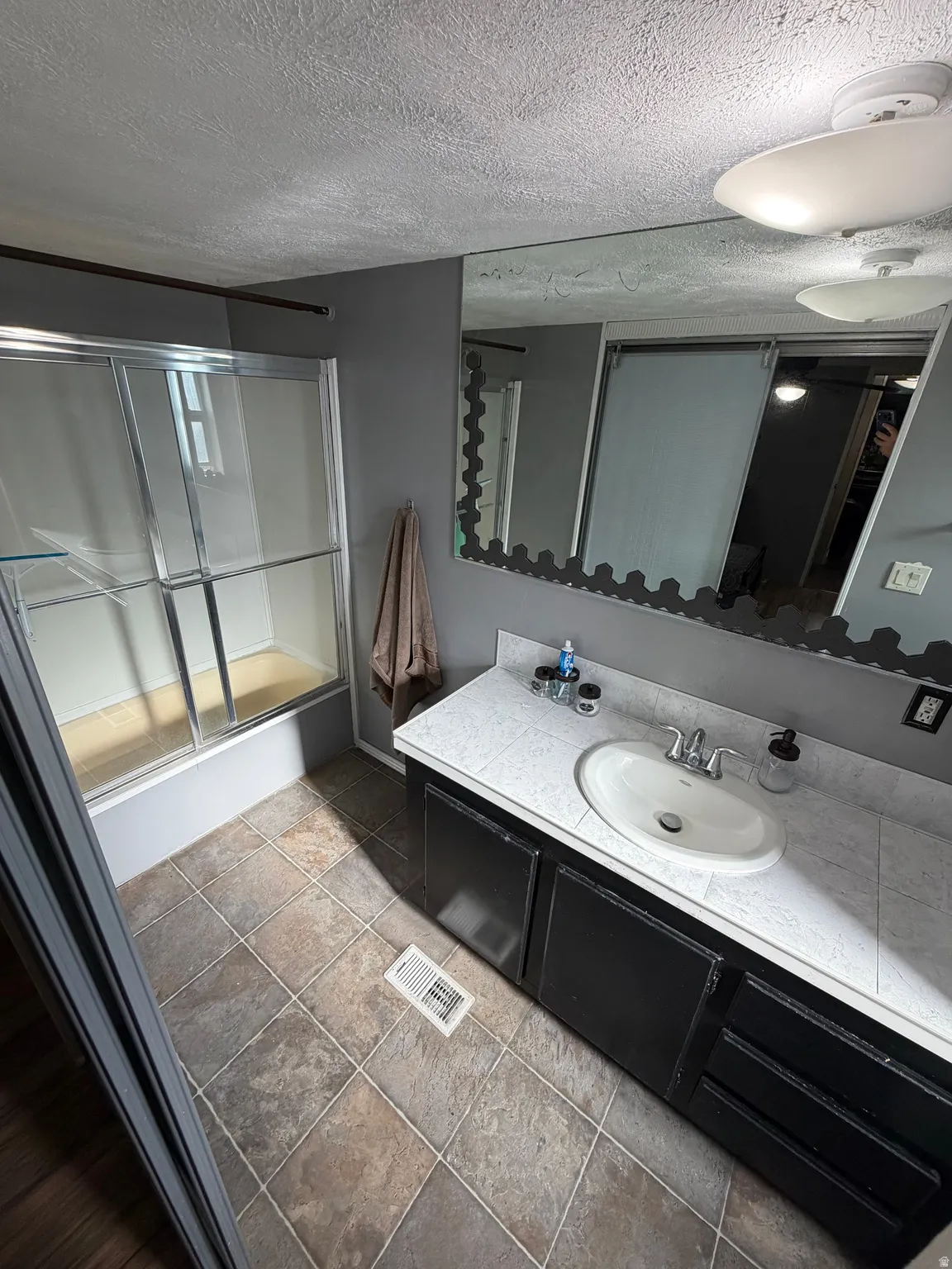 Tiled flooring with a single vanity featuring an integrated sink, a large wall-mounted mirror, and a shower with a sliding glass enclosure