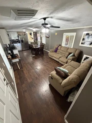Open-concept living space featuring wood-finish flooring, a ceiling fan with integrated lighting, and white trim accents