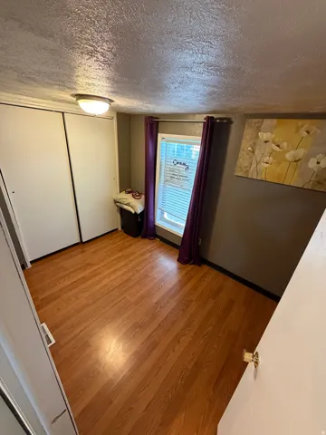 Wood-finish flooring with a ceiling-mounted light fixture, and a window with blinds