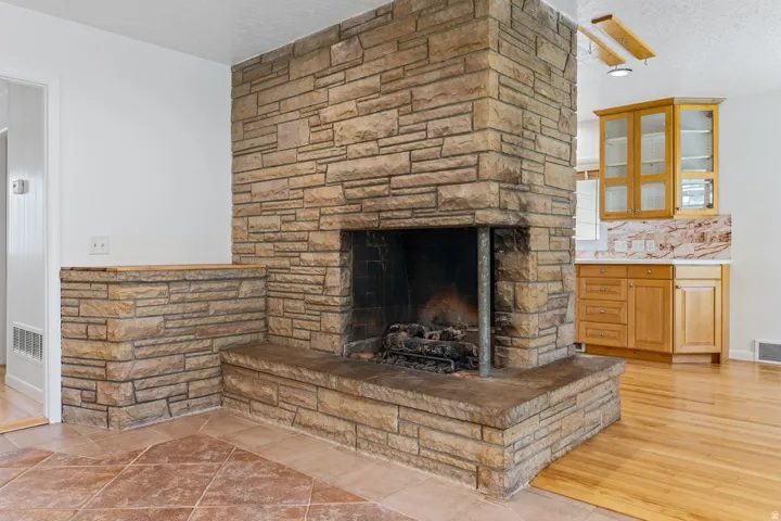Stone-clad fireplace with hearth, wood-finish flooring, and built-in cabinetry with glass doors