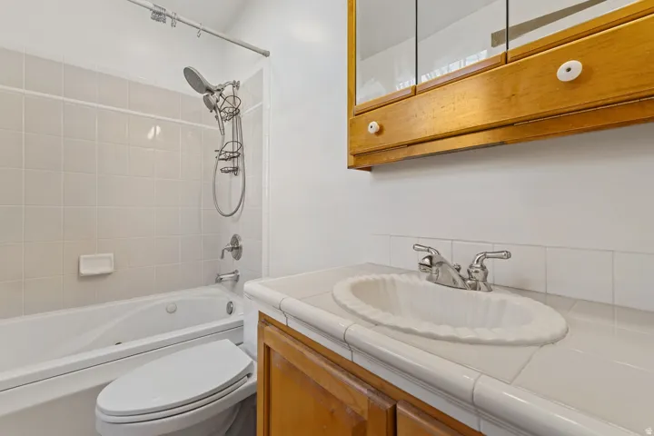 Wood-finish vanity, integrated white sink, chrome faucet, wood-frame medicine cabinet, and a tiled shower-over-tub combination