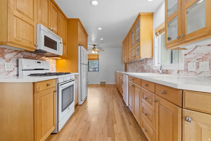 Wood-finish cabinetry, light-colored countertops, full tile backsplash, stainless steel sink with faucet, and recessed lighting
