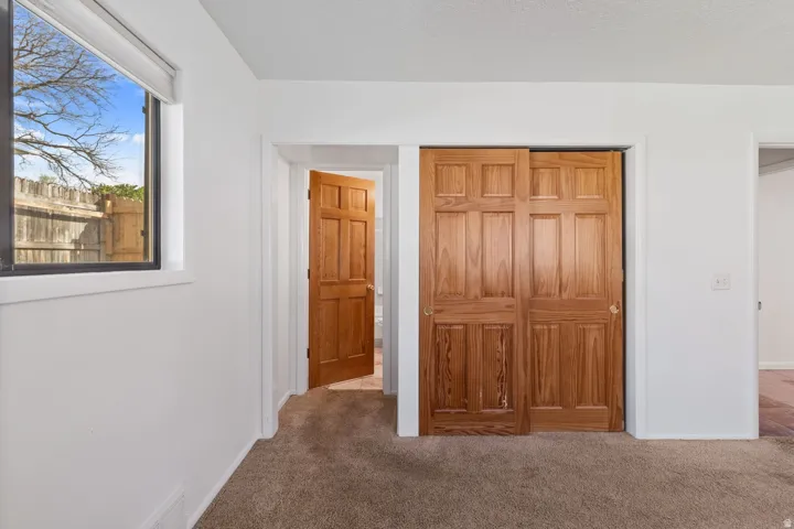 Recessed window with white trim, wood-paneled sliding closet doors, wood-paneled interior door, and neutral-toned carpeting