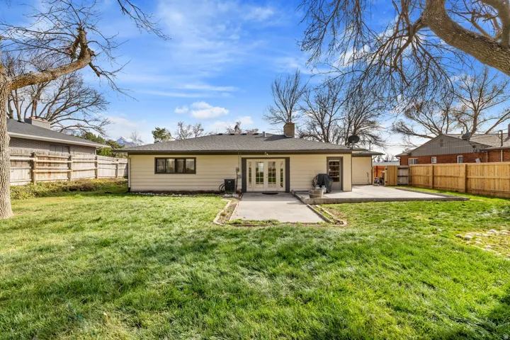 Expansive rear yard with a concrete patio, wood privacy fencing, and mature trees