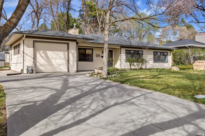 Single-story residence featuring light-colored siding, a dark roof, a garage, a concrete driveway, and a manicured lawn