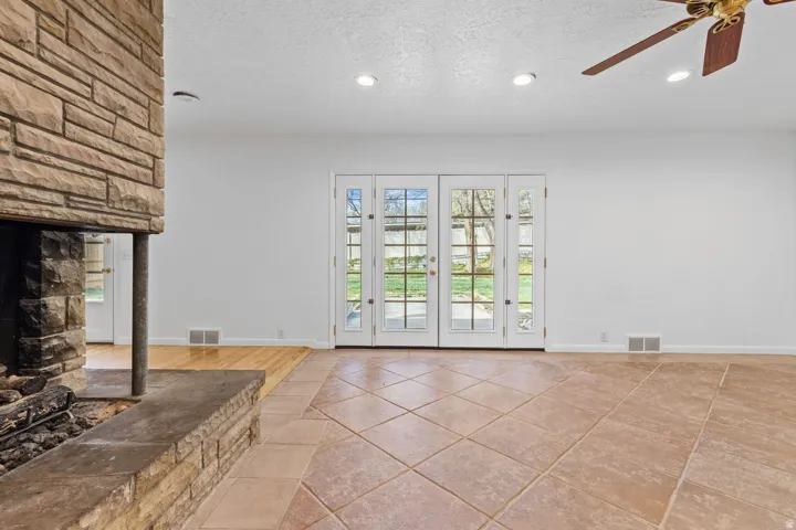 Stone-clad fireplace with a hearth, dual French doors with sidelights, recessed lighting, ceiling fan, and mixed flooring of tile and wood