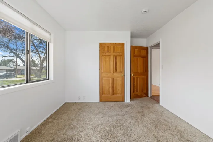 Light-colored carpeting, white painted walls, and a window with a roller shade