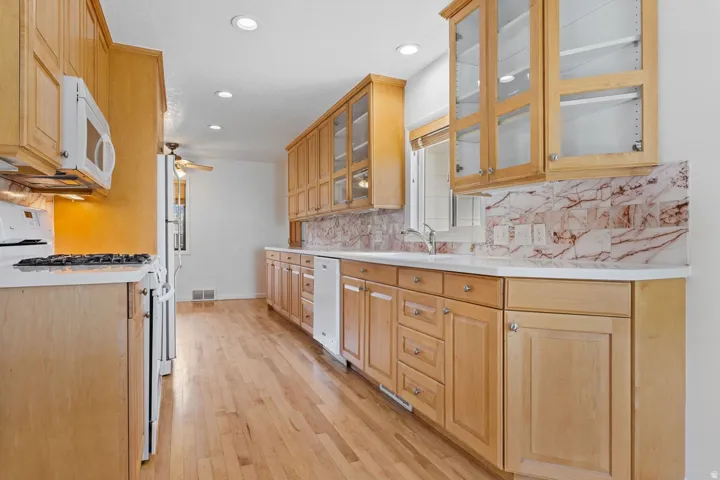 Wood-finish flooring, recessed lighting, wood cabinetry with glass fronts, white countertops, and a tile backsplash