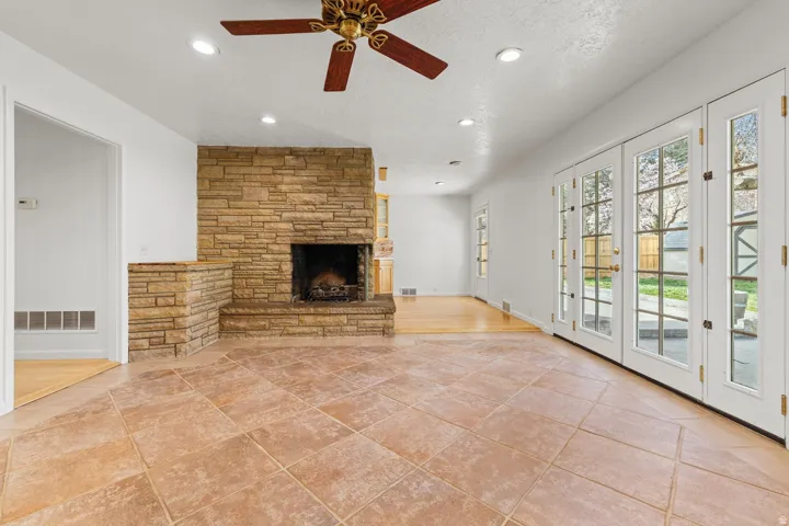 Stone-clad fireplace with hearth, tile flooring, recessed lighting, ceiling fan, and French doors leading to an outdoor patio