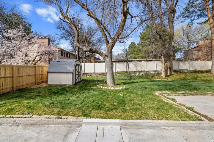Fenced yard space with a storage shed, mature trees, and a concrete perimeter