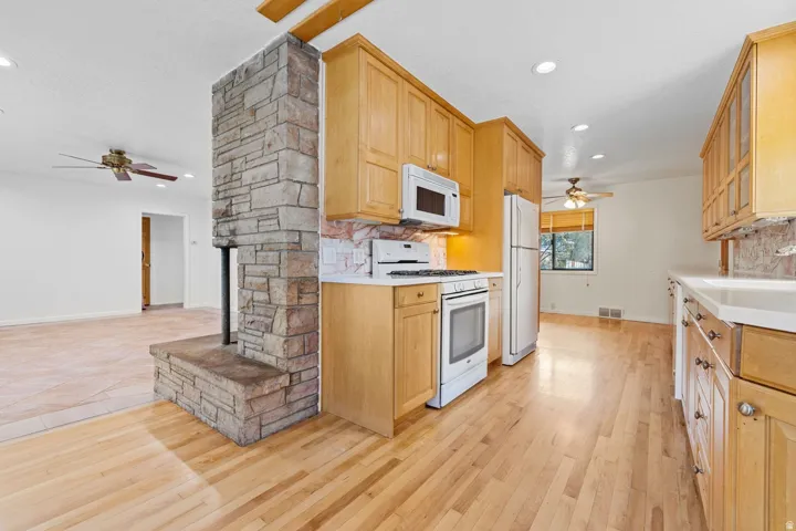 Wood-finish flooring, stone fireplace, light wood cabinetry, white appliances, and recessed lighting
