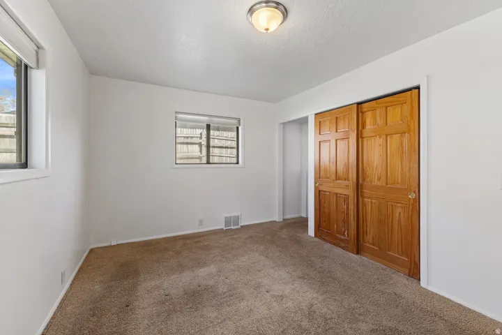 Neutral wall color, carpeted flooring, two windows, wood panel closet doors, and flush mount ceiling lighting