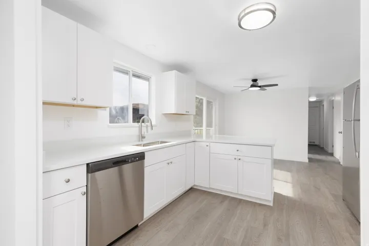 Kitchen featuring white shaker cabinetry, stainless steel dishwasher, an undermount sink, quartz countertops, and wood-finish flooring