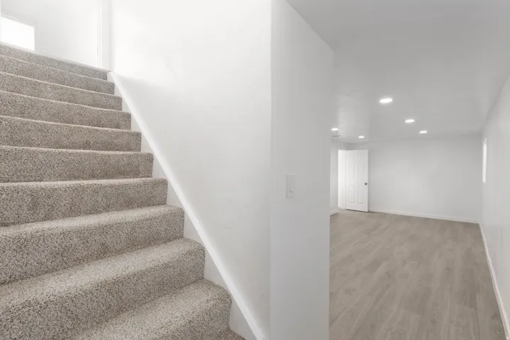 Carpeted staircase and a room featuring wood-finish flooring, recessed lighting, and white walls