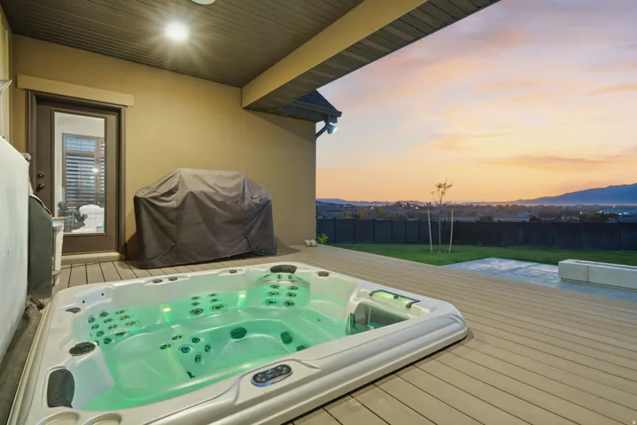 Outdoor spa with integrated lighting, composite decking, covered patio, and a landscaped yard