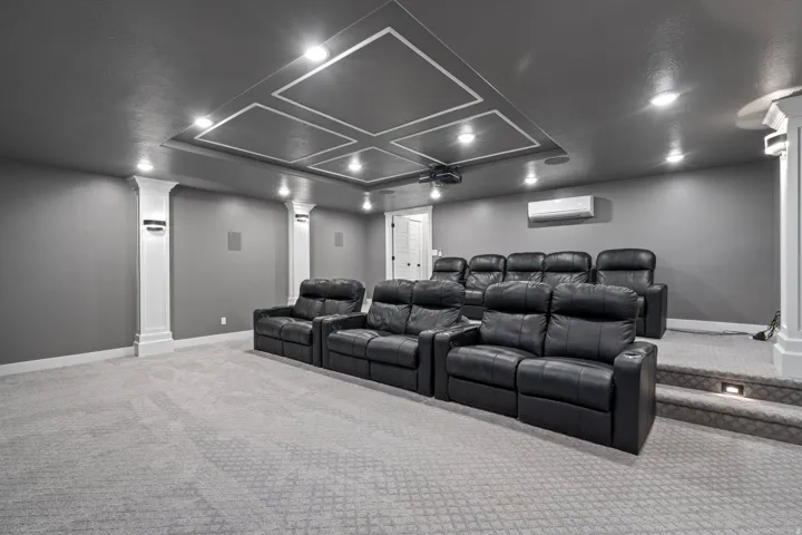 Theater room featuring tiered seating, recessed lighting, coffered ceiling detail, and built-in wall speakers