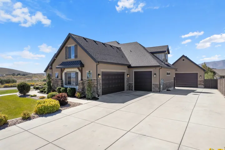 Stucco exterior with stone accents, a dark shingle roof, multiple dark garage doors, concrete driveway, and landscaped front yard