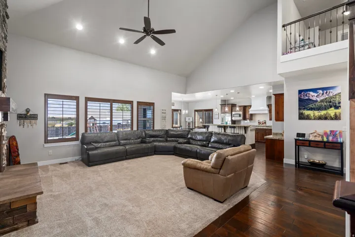 Vaulted ceiling with recessed lighting, stone-clad fireplace, dark wood-finish flooring, and a kitchen with warm wood cabinetry