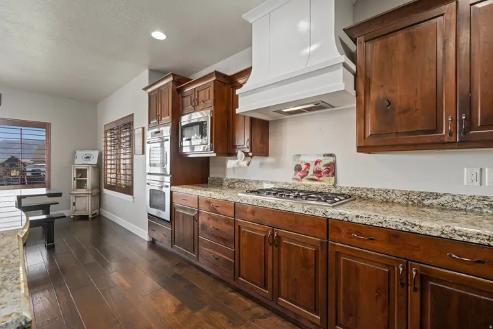 Dark wood-finish flooring, rich wood cabinetry, light-toned countertops, stainless steel appliances, and a white range hood