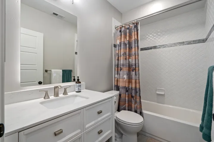 Vanity with integrated sink, brushed nickel faucet, large wall mirror, and tiled shower with decorative accent band