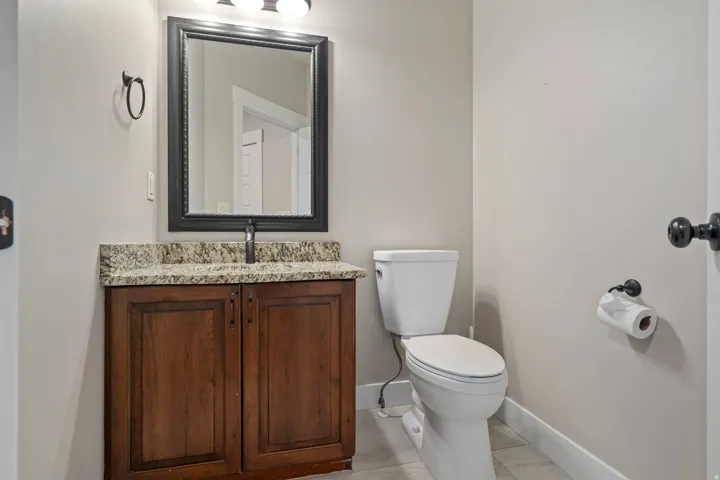 Wood-finish vanity with a stone countertop, framed mirror, and a white toilet