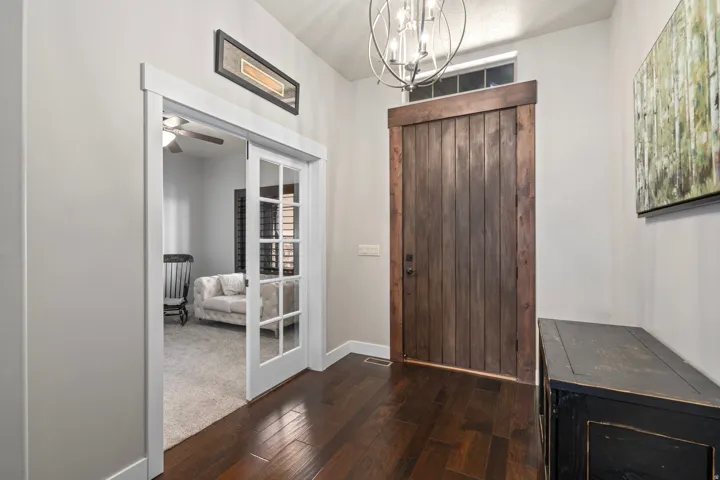 Rich wood-finish flooring, a rustic wood paneled door with transom window, and a contemporary chandelier