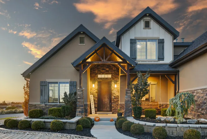 Exterior featuring stone accents, board and batten siding, dark wood shutters, a covered entry with exposed wood beams, and structured landscaping