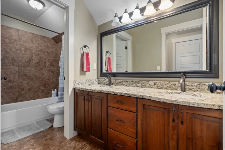 Double vanity with stone countertop, dark wood-finish cabinetry, and framed mirror