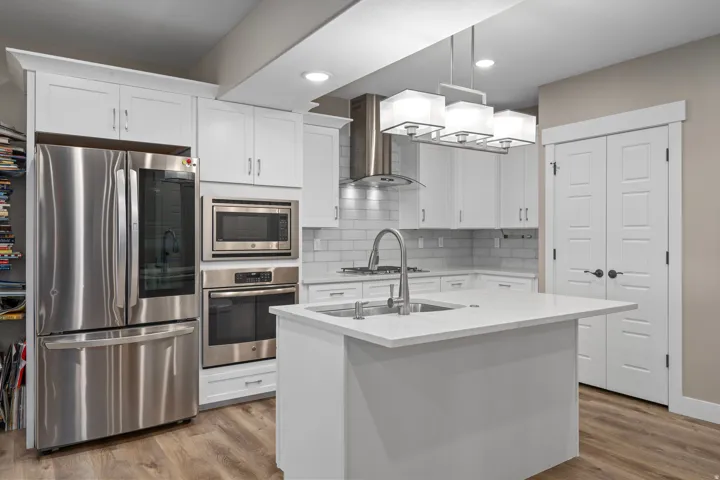 White shaker cabinetry, stainless steel appliances, central island with sink, subway tile backsplash, and wood-finish flooring