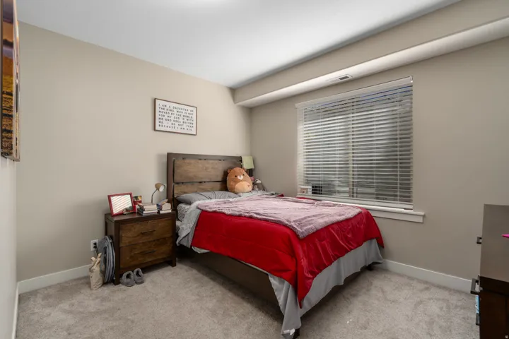 Carpeted bedroom featuring a window with blinds, light-toned walls, and a flat ceiling