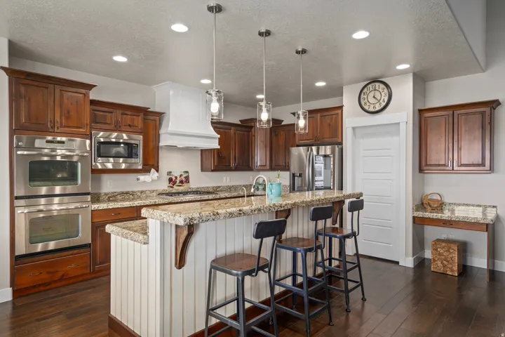 Kitchen featuring wood-finish flooring, wood cabinetry, granite countertops, stainless steel double ovens, and a built-in microwave