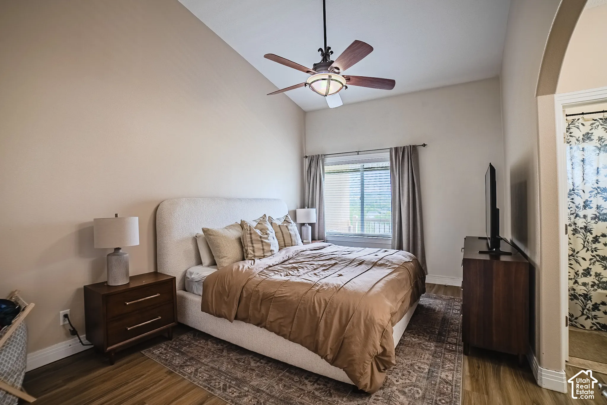 Vaulted ceiling with a ceiling fan, wood-finish flooring, and a large window with blinds
