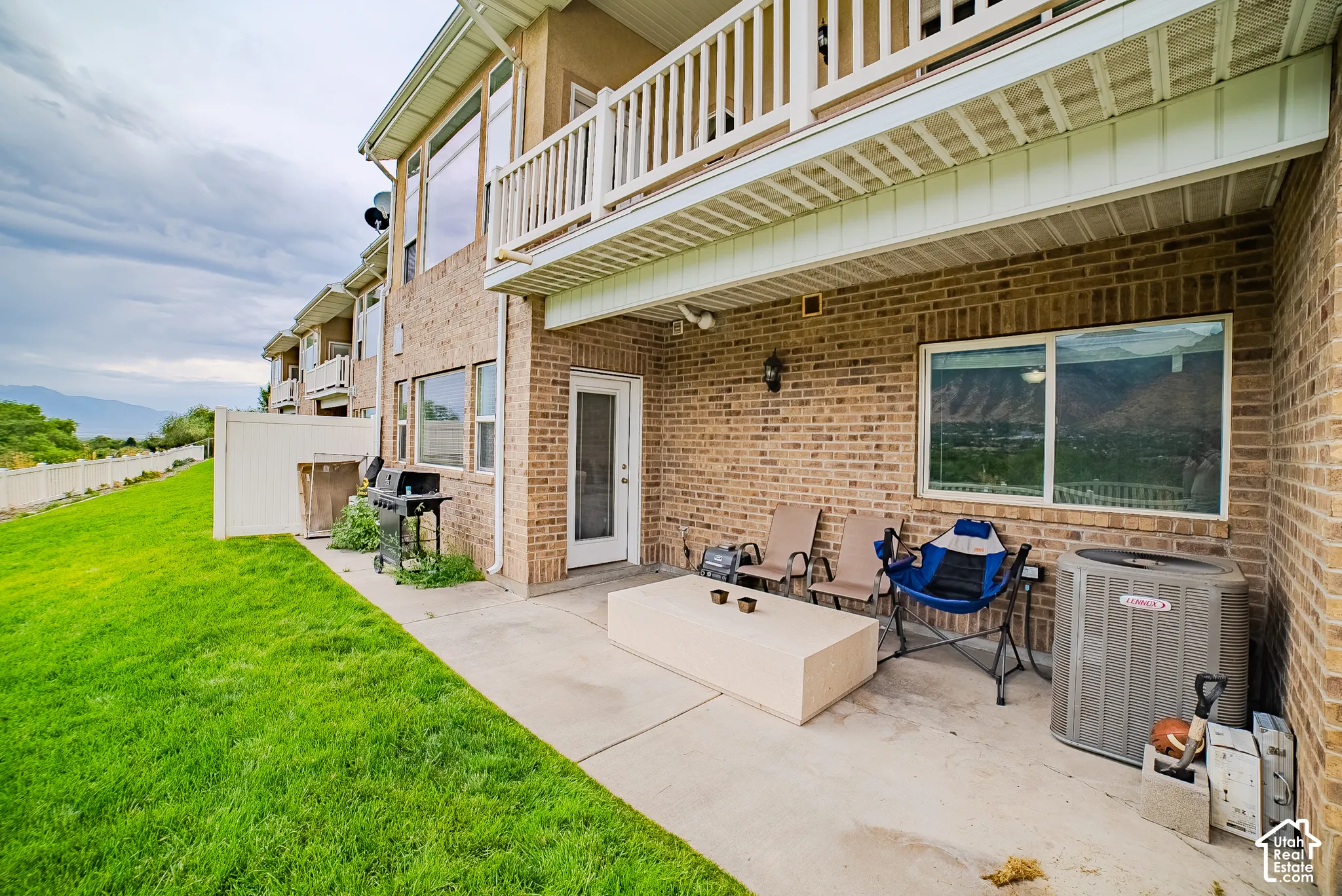 Brick exterior with a ground-level patio, upper-level balcony, and a manicured lawn