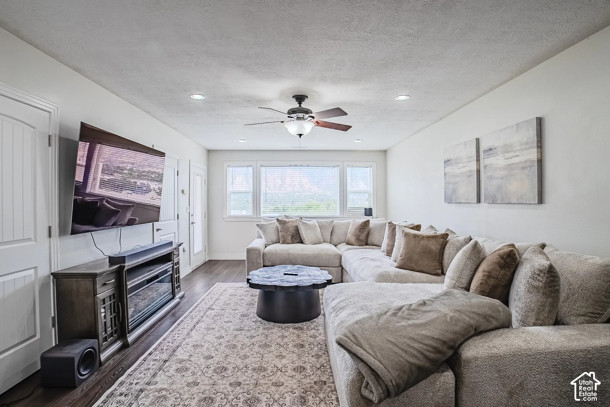 Recessed lighting throughout, ceiling fan with light fixture, multiple windows providing natural light, wood-finish flooring, and built-in media console with electric fireplace