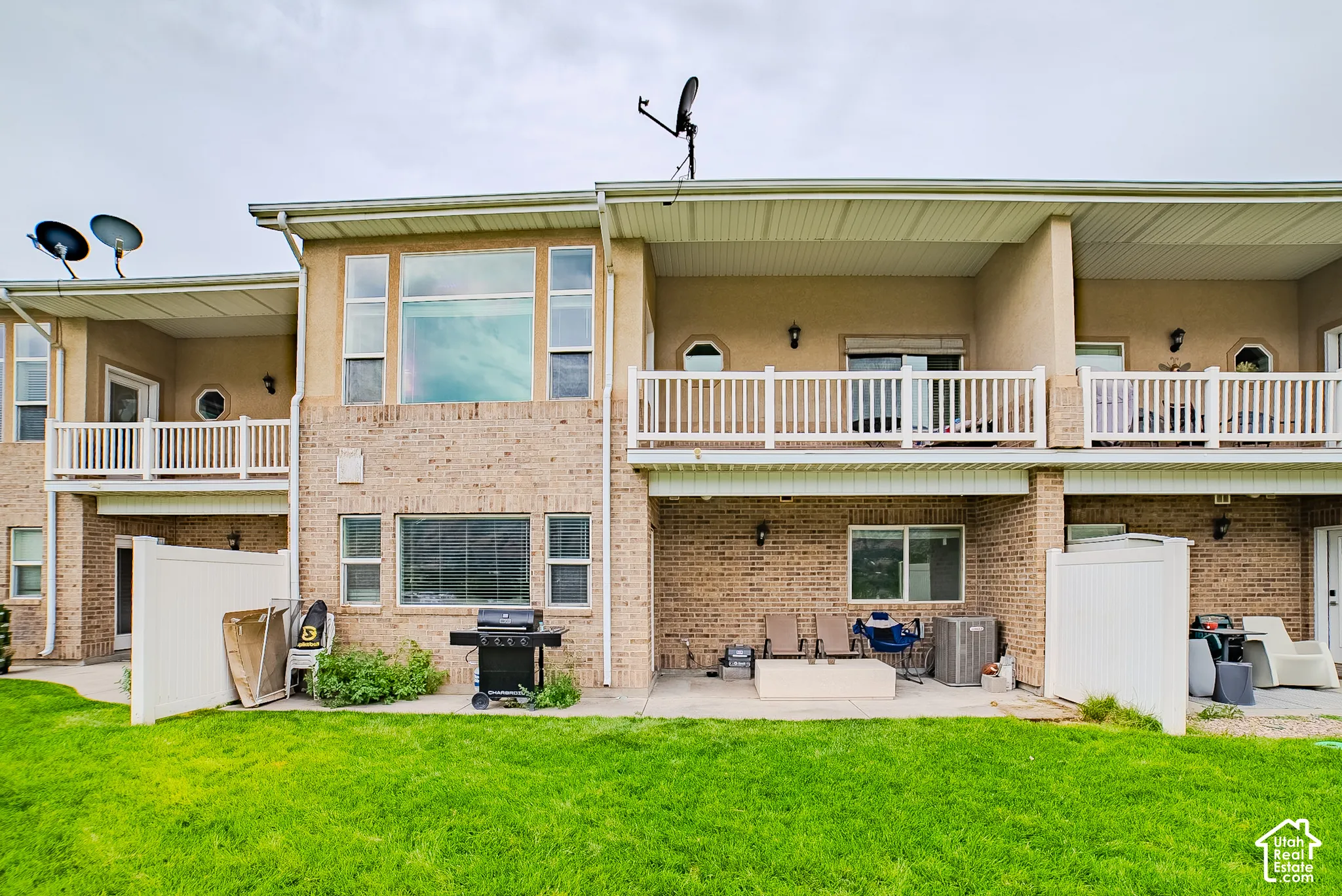 Brick and stucco exterior with multiple balconies, a ground-level patio, and a grassy yard