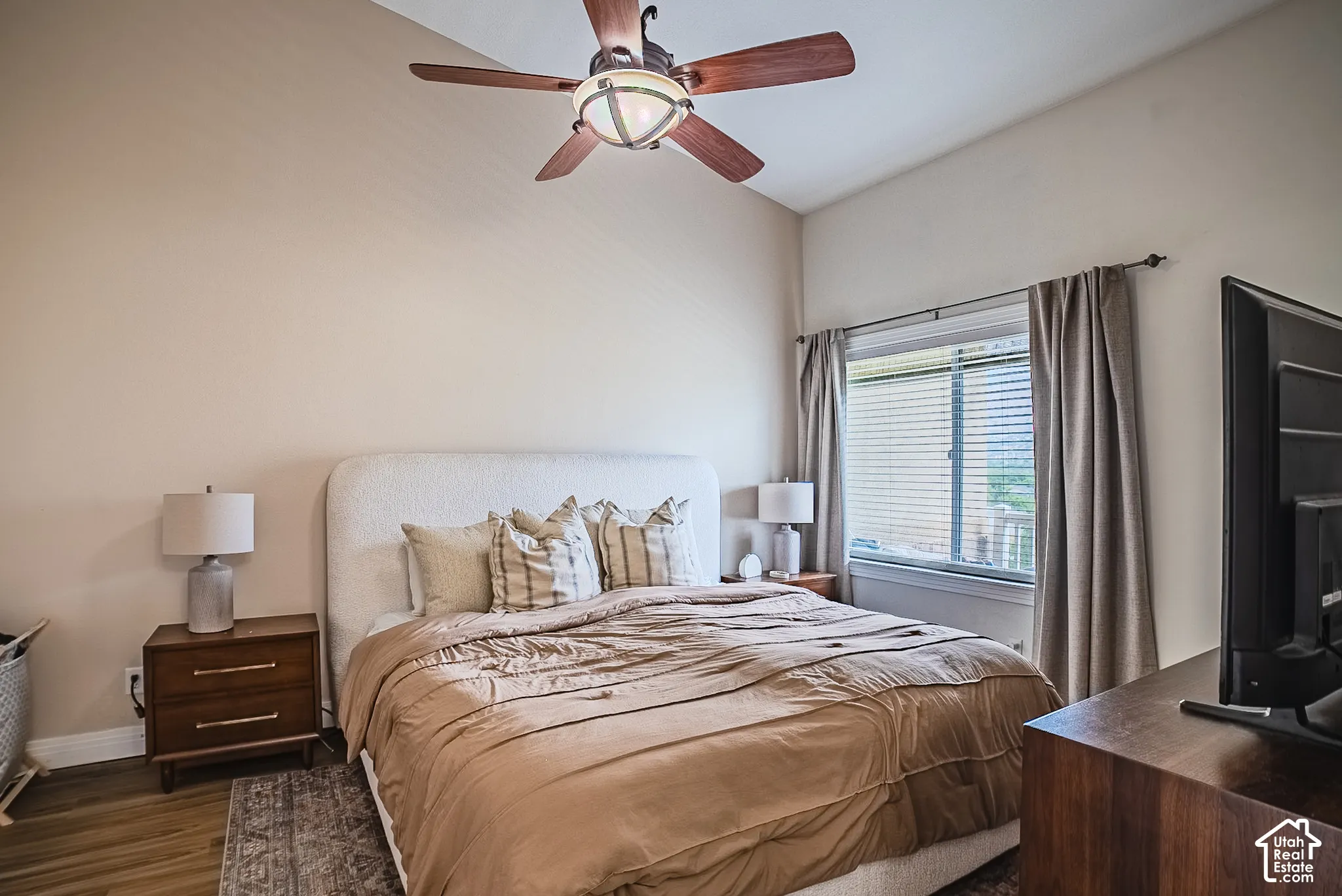 Vaulted ceiling with a wood-blade ceiling fan, wood-finish flooring, window with blinds and drapes, and a built-in wood-tone dresser