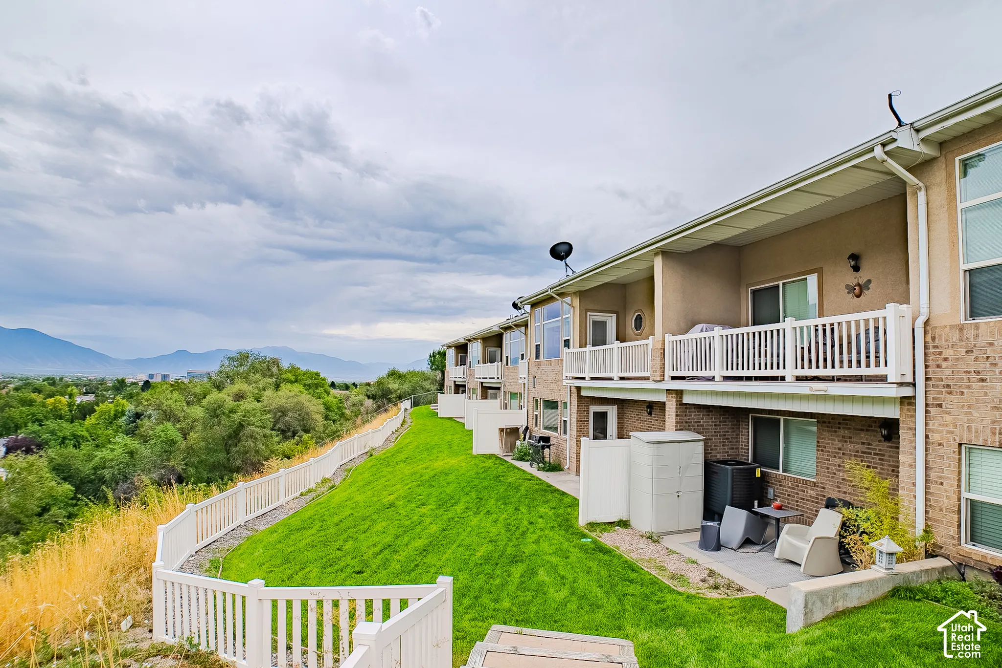 Terraced property with private balconies, ground-level patios, expansive green space, and white picket fencing