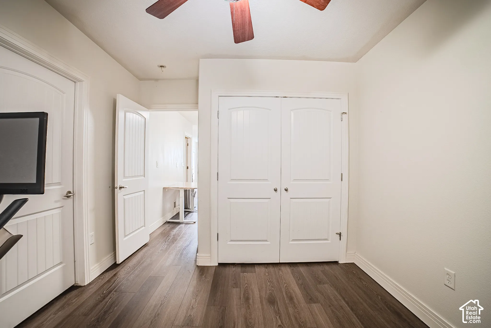 Wood-finish flooring, white paneled doors, ceiling fan with wood-tone blades, and a built-in closet with double doors