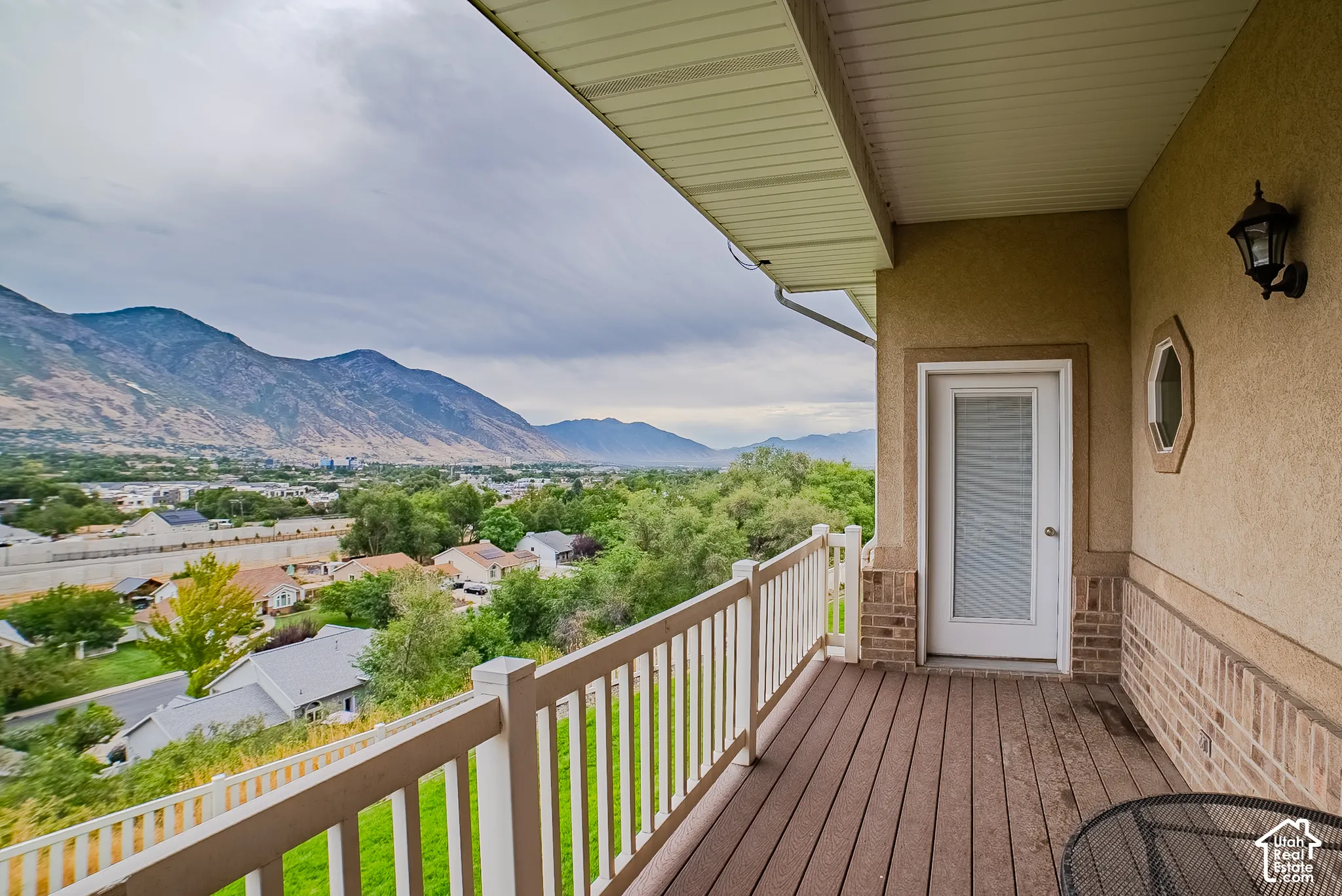 Private balcony featuring composite decking, white railing, and exterior wall sconce