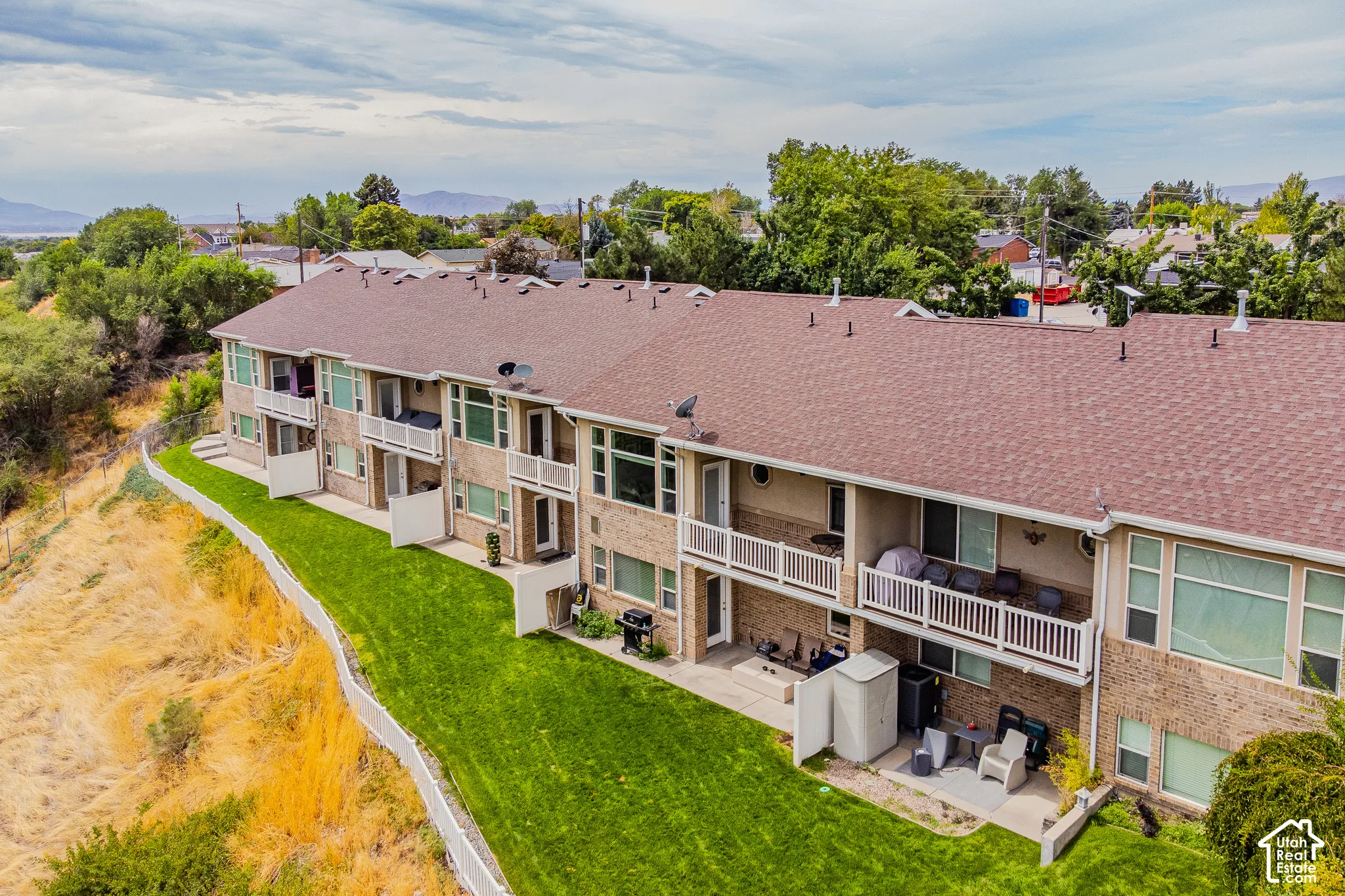 Brick exterior with multiple private balconies, ground-level patios, expansive green lawn, and a shingle roof