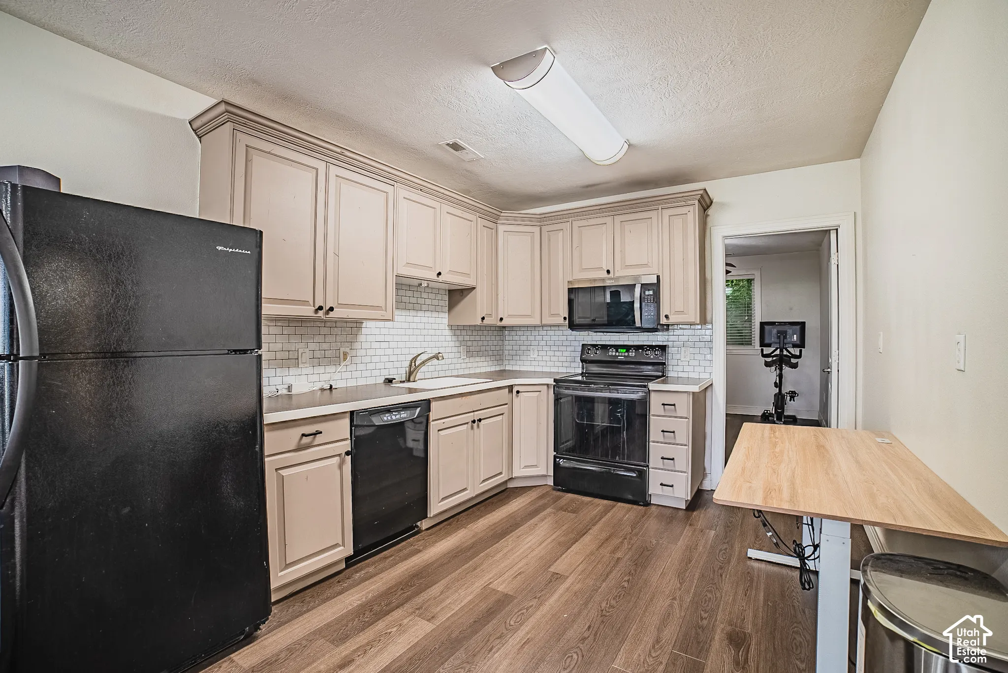 Kitchen featuring wood-finish flooring, light-toned cabinetry with crown molding, stainless steel sink, white subway tile backsplash, and black appliances
