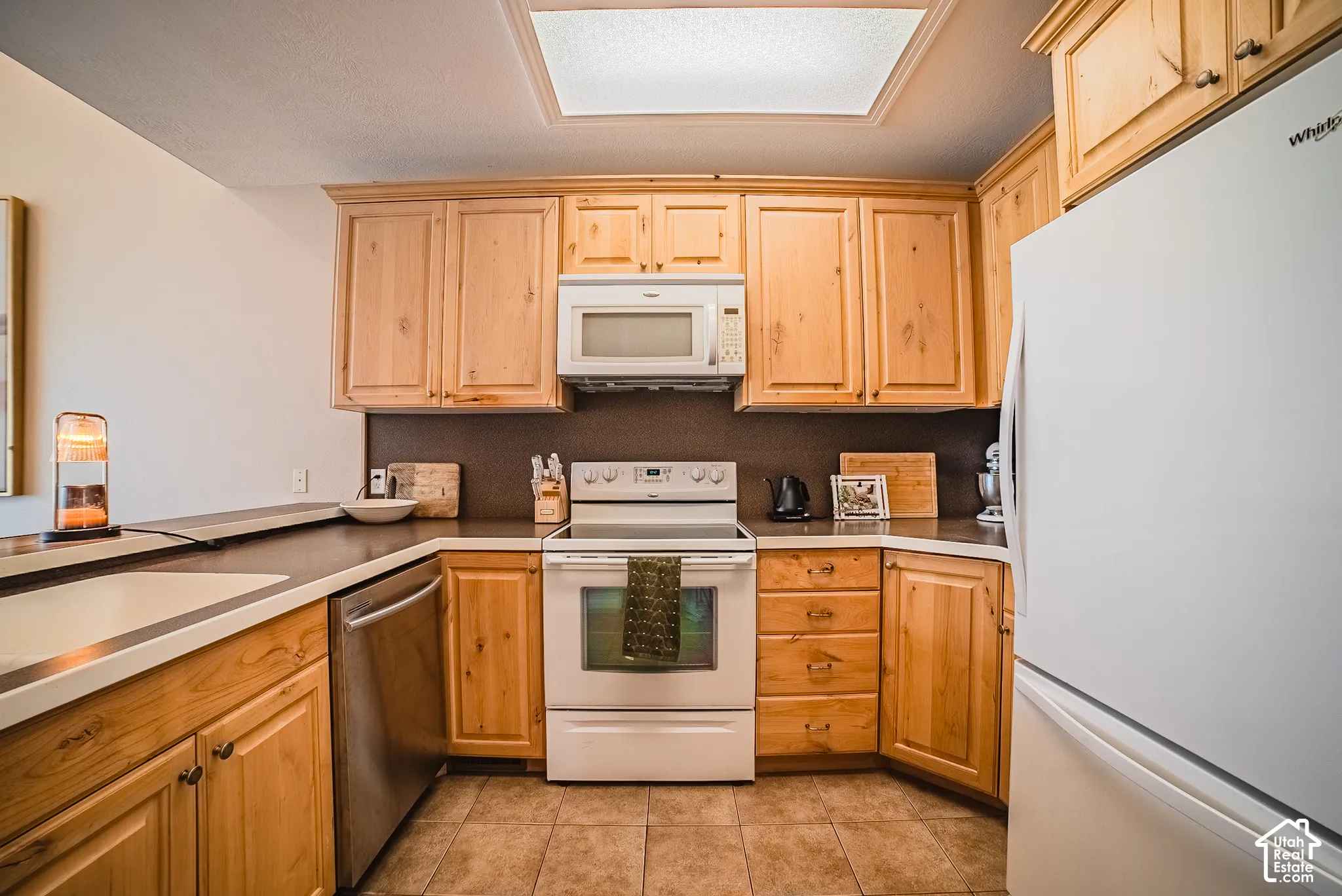 Kitchen featuring wood-finish cabinetry, tile flooring, and integrated white appliances